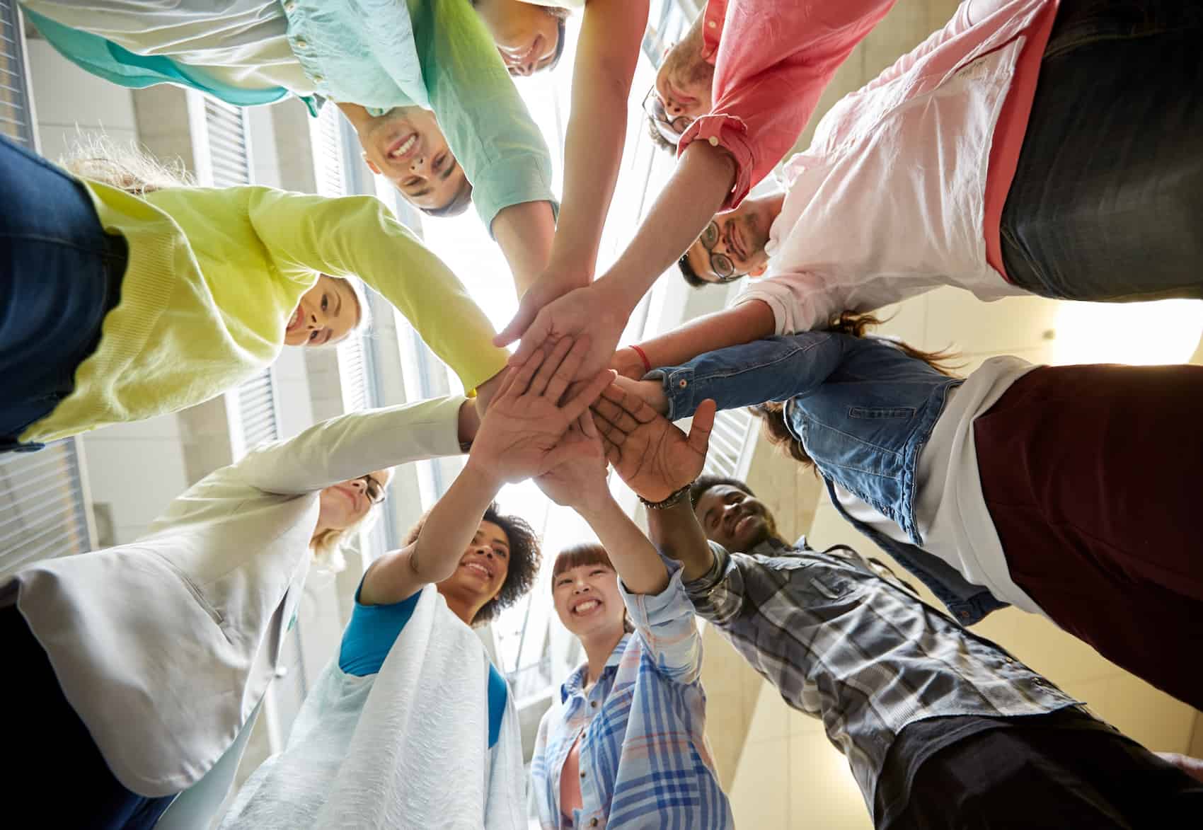 education, school, teamwork and people concept - group of international students with hands on top of each other over table